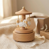 Sheep musical carousel on a cream knit blanket beside a kraft gift box with ivory ribbon