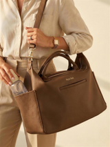 Mother carrying the Wyld Bub diaper bag over her shoulder, slipping a bottle into the side pocket