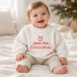 Baby wearing the white speckled personalised first Christmas sweater beside a Christmas tree